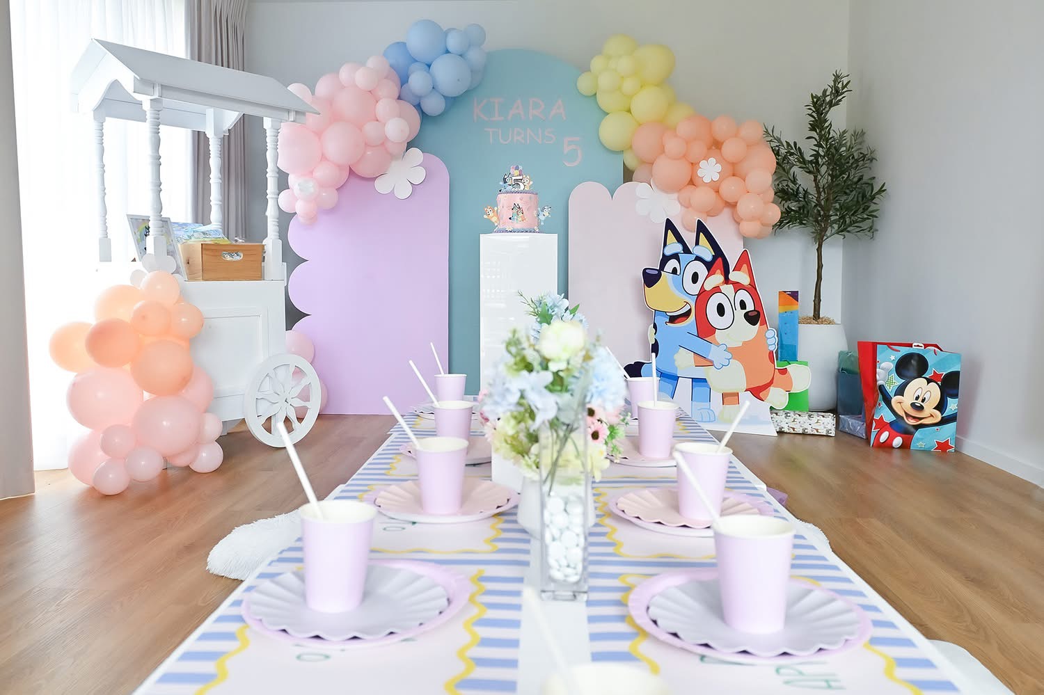 Bluey themed fifth birthday party table setting with pastel balloon arches