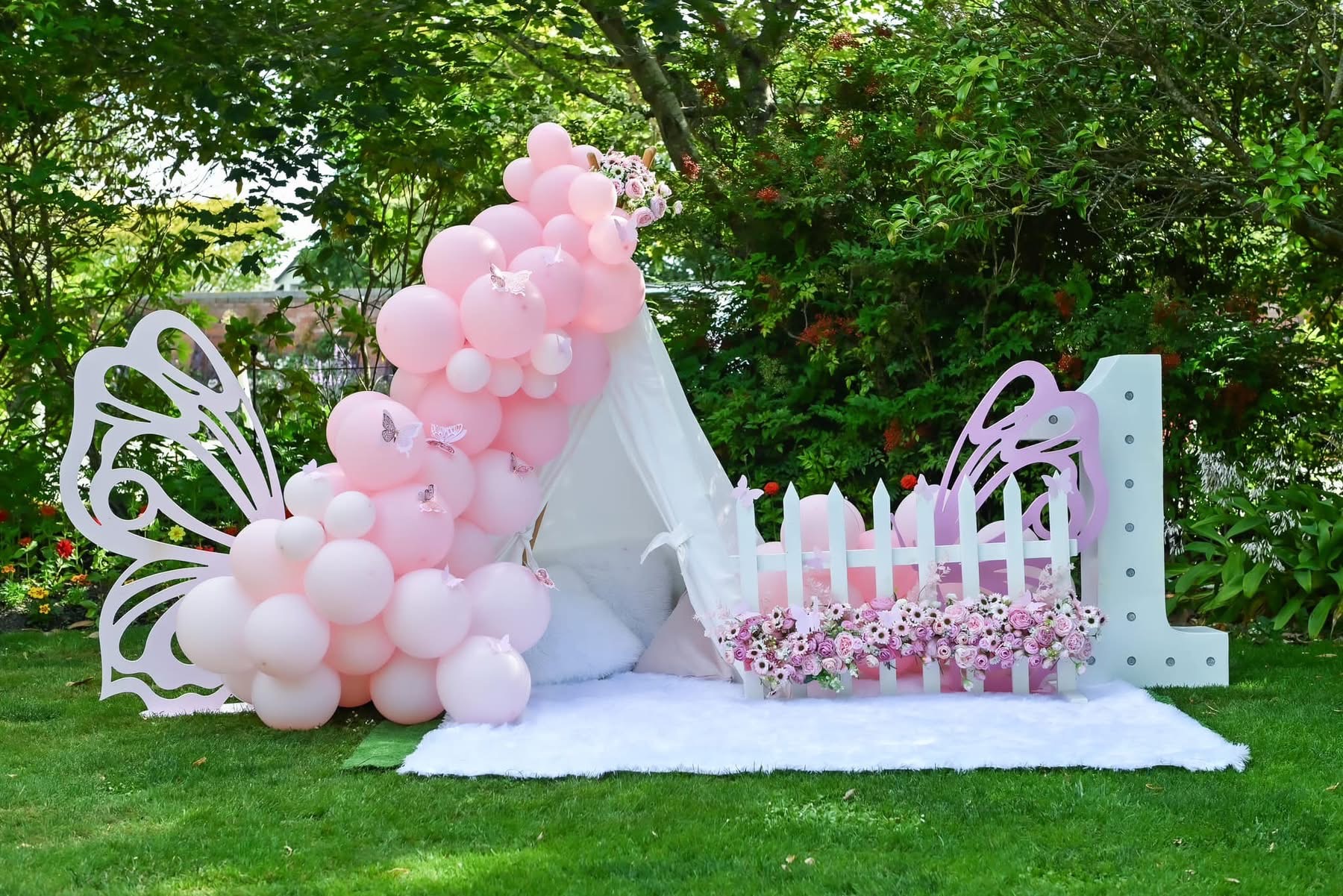 Pink balloon garland with butterfly cut-outs and a garden teepee backdrop